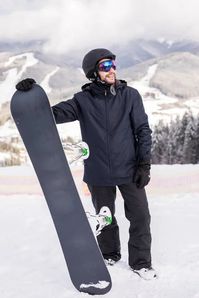 Snowboardzista przytrzymaj snowboard na szczycie wzgórza w pobliżu portret, śnieg na szczytach snowboardzie na stokach. Ośrodek narciarski. — Zdjęcie stockowe