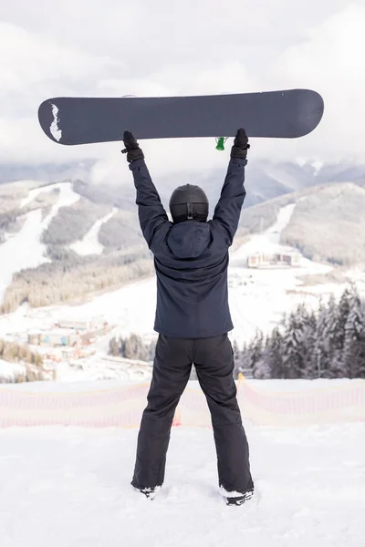 Glücklicher Mann, der mit Snowboard über dem Kopf auf dem Gipfel des Berghügels steht — Stockfoto