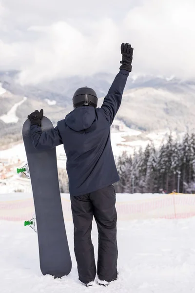 Vista trasera del deportista con snowboard observando la naturaleza con la mano arriba —  Fotos de Stock