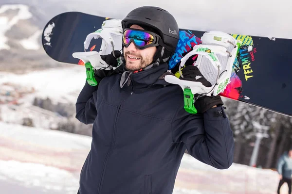 Snowboardzista, relaksujące i pozowanie w słoneczny dzień w ośrodku ske z snowboard nad głową. Czas zimowy. — Zdjęcie stockowe