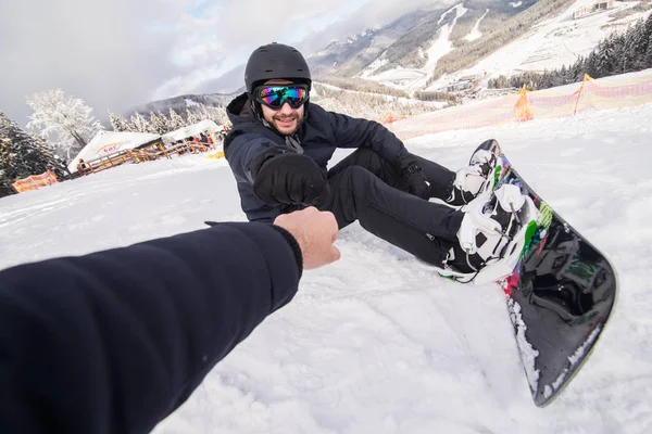 Snowboarder schnallt Snowboardschnallen sitzend auf der Spitze des Schneehügels an und gibt fünf — Stockfoto