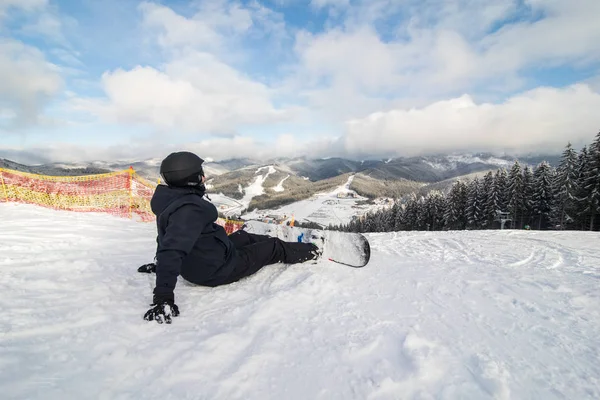 Snowboardista leží vysoko v horách na okraji svahu a dívá do dálky stopy — Stock fotografie