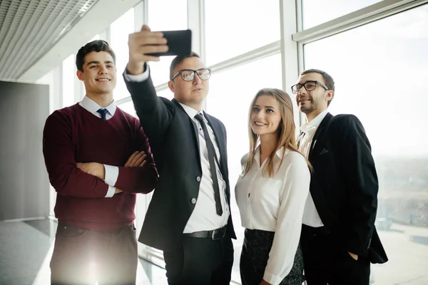 Happy co-workers makes selfie. Three laughing young business people makes selfie with the sell phone in office