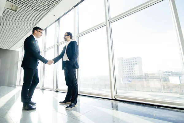 Vista lateral completa de los hombres de negocios estrechando la mano en las ventanas de la oficina . — Foto de Stock