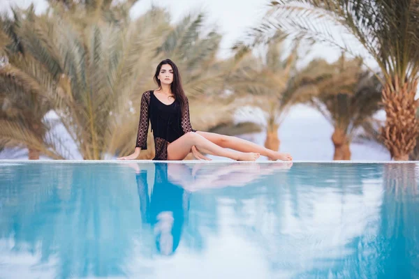 Hermosa mujer de vacaciones relajándose en un balneario tropical tumbada en el borde de la piscina infinita tomando el sol en su bikini contra un telón de fondo de palmeras . —  Fotos de Stock