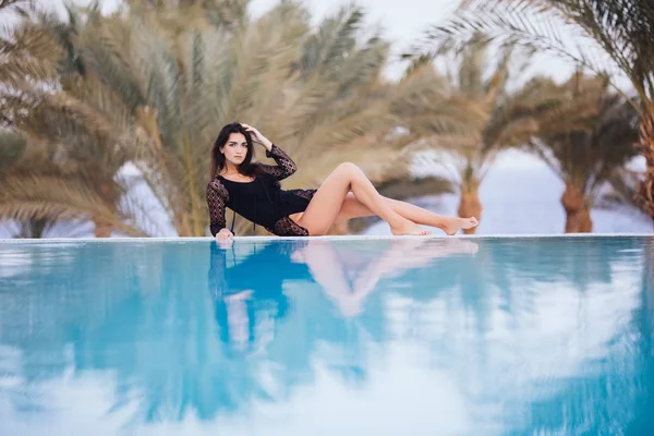 Gyönyörű nő pihentető egy trópusi spa Resort, feszített víztükrű medencével, napozó lány bikini pálmafák a háttérben szélén fekvő. — Stock Fotó
