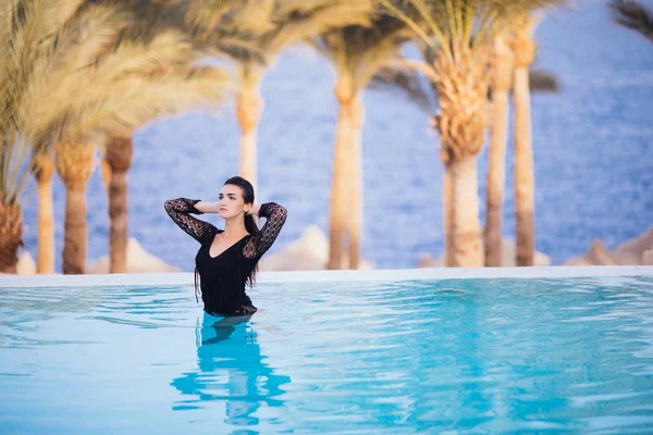 Hermosa chica es relajarse en una piscina infinita en vista de verano —  Fotos de Stock