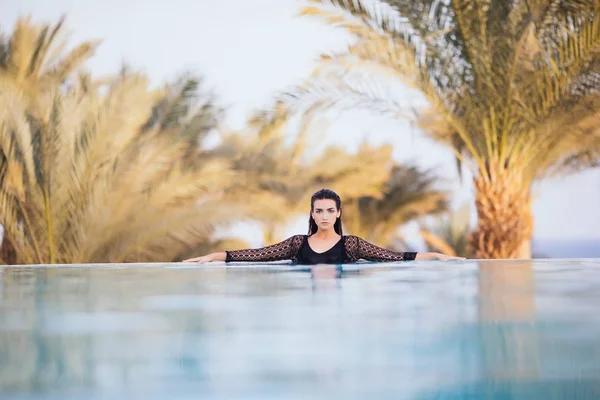 Chica en la piscina infinita en el hotel de la azotea relajarse en el agua sobre el mar y las palmas de fondo —  Fotos de Stock