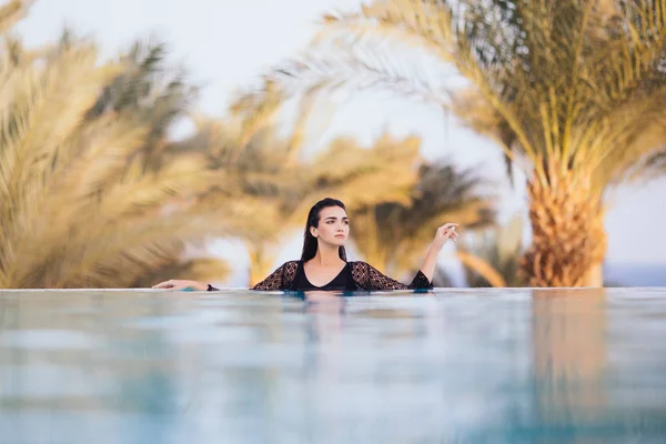 Chica en la piscina infinita en el hotel de la azotea relajarse en el agua sobre el mar y las palmas de fondo —  Fotos de Stock