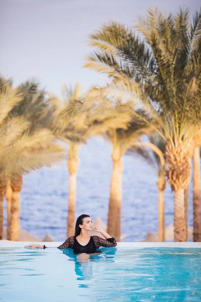 Портрет брюнетка женщина расслабиться в воде бесконечности бассейн с руками на краю роскошный курорт, бесконечный вид на море — стоковое фото