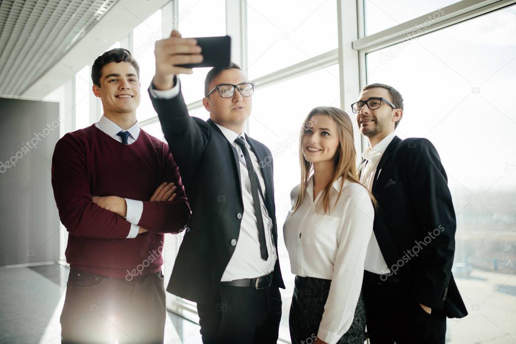 Happy co-workers makes selfie. Three laughing young business people makes selfie with the sell phone in office