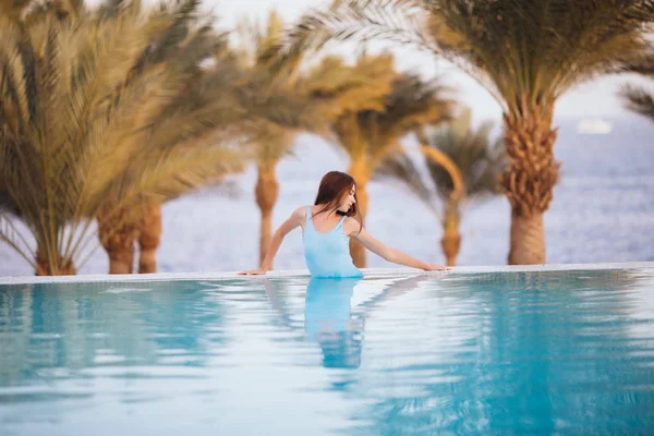 Szép szexi nő pihentető víztükrű medencével, pálmák és tengeri háttér — Stock Fotó