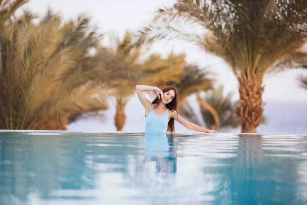 Σέξι γυναίκα ομορφιά με μαγιό ποζάρει και να χαλαρώσετε στην πισίνα με φοίνικες και θάλασσα σε φόντο στο luxury resort. Καλοκαίρι κλίση, ταξίδια, περιπέτεια. — Φωτογραφία Αρχείου