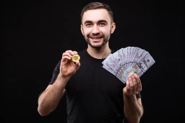 Genç yakışıklı adam siyah arka plan üzerine izole diğer elinde dolar nakit ve altın bitcoin ile