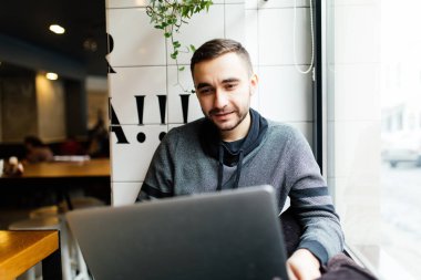 Bir kafede bir dizüstü bilgisayar ile bir genç adam. Serbest çalışan,