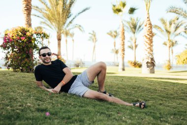 Yaz aylarında çim sahası egzotik bir bahçe içinde yatan mutlu genç adam. Yaz meslek