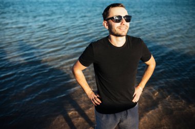 Deniz suyunda t-shirt ve şort giyen sahilde gülümseyen adam