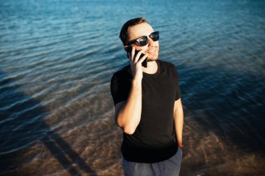 Yakışıklı genç deniz sahilde cep telefonu ile konuşurken güneş gözlüğü