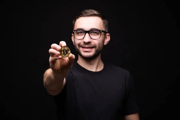 Siyah gömlekli gözlüklü genç yakışıklı adam altın bitcoin siyah arka plan üzerine izole kamera işaret etti — Stok fotoğraf