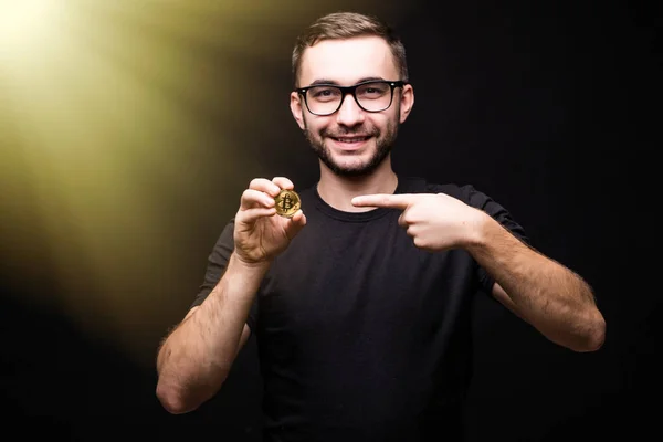 Retrato de hombre joven en gafas de desgaste en camisa negra apuntado en bitcoin aislado sobre fondo negro —  Fotos de Stock