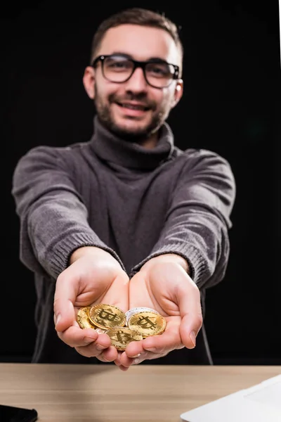 Portrét muže v brýlích ukazuje zlatá bitcoiny ve svých rukou na stůl izolované černém pozadí — Stock fotografie