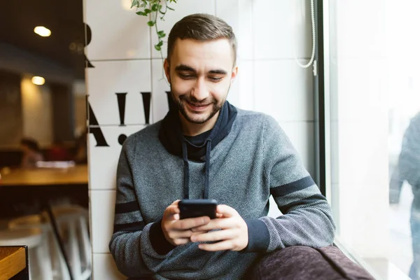 Cep telefonu kafede kullanan çekici adam yakışıklı genç gülümsemek — Stok fotoğraf