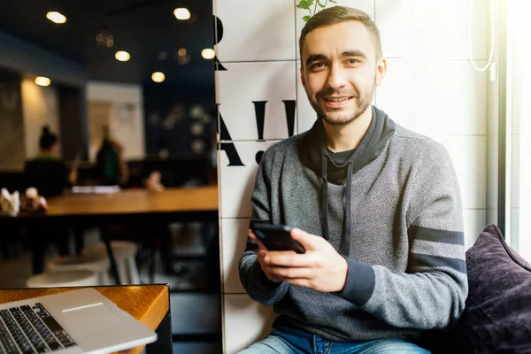Wohlhabende männliche Unternehmer senden Nachrichten und Multimedia-Dateien auf dem Smartphone arbeiten im Café. Erfahrener Marketingmanager synchronisiert Telefondaten mit Laptop-Sharing-Fotos für Projekt — Stockfoto