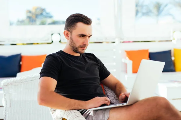 Hombre joven con ordenador portátil en la cafetería al aire libre en las vacaciones de verano — Foto de Stock