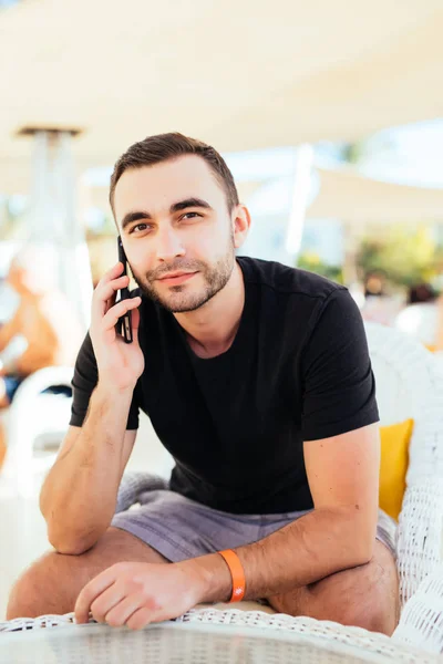 Junger Mann, der auf der Terrasse am Meer mit dem Smartphone spricht. Sommerberuf. — Stockfoto