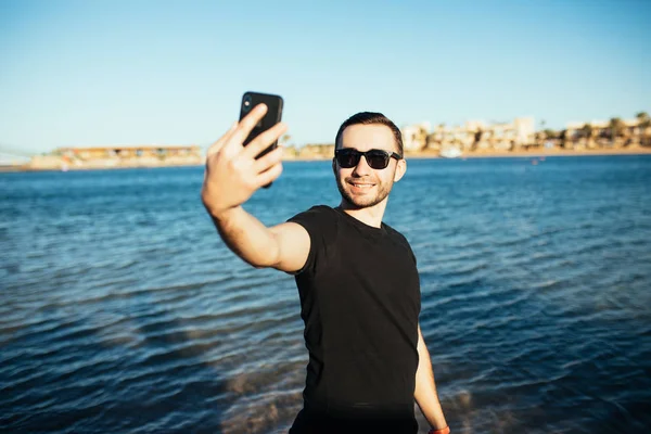 Jovem homem bonito fazendo um auto-retrato com smartphone no fundo da praia do mar — Fotografia de Stock