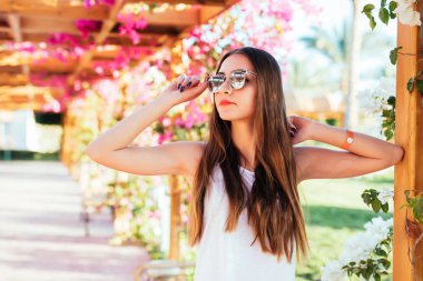 Esmer uzun saçlı kız şort, whitet-gömlek ve güneşli bir hava bir kafede bir bankta trendy güneş gözlüğü ile.