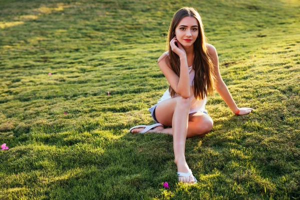 Brązowe włosy dziewczyna spędzania wolnego czasu, siedząc na trawie w parku, zrelaksować się na słońcu — Zdjęcie stockowe