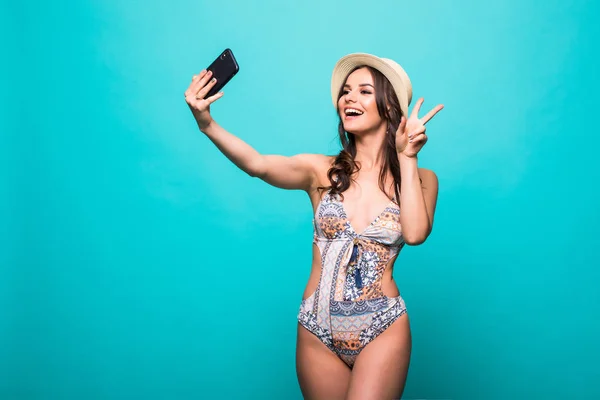 Carino bruna donna in bikini facendo selfie con segno di vittoria indossare cappello di paglia isolato su sfondo verde — Foto Stock