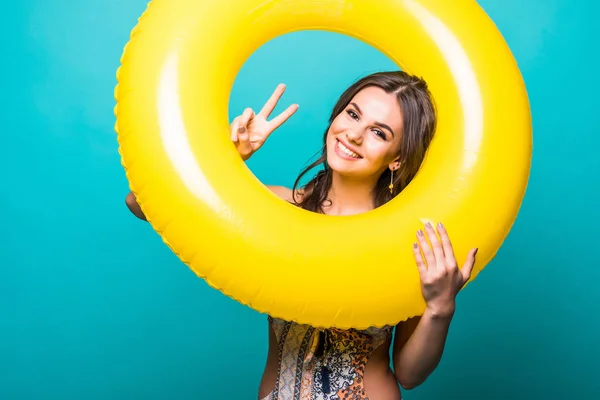 Gros plan portrait d'une belle femme en bikini regarder à travers grand anneau gonflable jaune et montrer le signe de victoire à la caméra sur fond vert — Photo