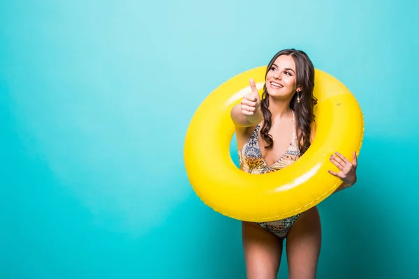 Beauté jeune femme en maillot de bain avec un anneau gonflable et la main montrant pouces geste isolé sur fond vert — Photo