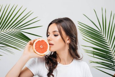 Yeşil yaprakları ile poz ve holding esmer saçlı gülümseyen bir kadın portresi beyaz arka plan üzerinde izole greyfurt dilimlenmiş