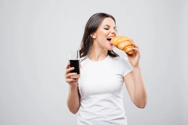 Portret piękny Ładna dziewczyna jedzenia rogalika i picia coli ze szkła na białym tle nad białym tle — Zdjęcie stockowe