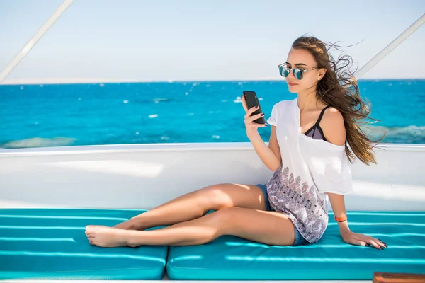 Gyönyörű fiatal barna lány telefont ülve, a yacht — Stock Fotó