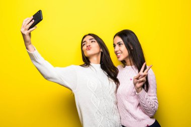 İki neşeli kız portresi duran ve üzerinde sarı arka plan izole bir selfie alarak Kazak giymiş
