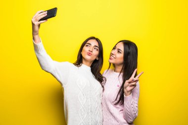 İki neşeli kız portresi duran ve üzerinde sarı arka plan izole bir selfie alarak Kazak giymiş