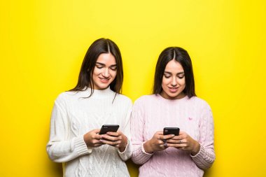 Chat yapan iki neşeli kız sarı arka plan üzerinde izole fotoğraf.