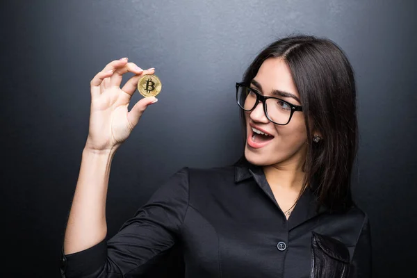 Młody udane przekonana kobietę w okularach w ręku na białym na czarnym tle trzyma złoty bitcoin — Zdjęcie stockowe