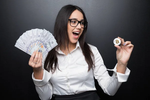 Joven mujer de negocios exitosa sosteniendo un bitcoin de oro y dinero en efectivo aislado sobre fondo negro —  Fotos de Stock