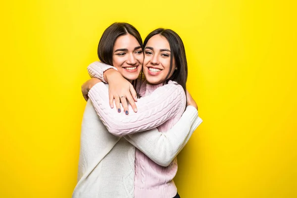 Retrato de dos chicas felices vestidas con suéteres abrazándose aisladas sobre fondo amarillo — Foto de Stock