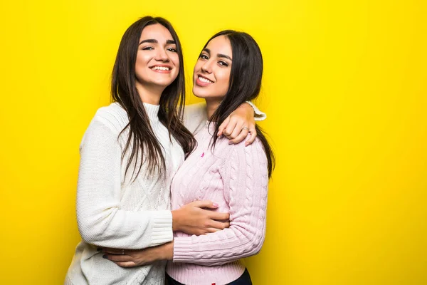 Retrato de duas meninas felizes vestidas com suéteres abraçando isolado sobre fundo amarelo — Fotografia de Stock