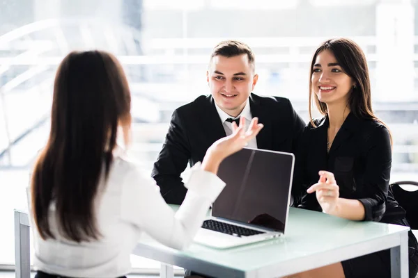 Een contract met de beste voorwaarden. Zeker jonge vrouw uitleggen enkele details van document en wijzen het met glimlach terwijl u zit samen met jong koppel aan de balie in kantoor — Stockfoto