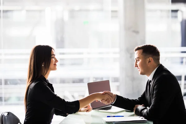 Empresaria y hombre de negocios estrechando las manos sobre la mesa con el ordenador portátil y los papeles en la oficina, agradable reunión de negocios, iniciar la negociación . — Foto de Stock