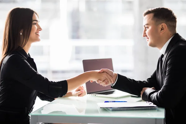 Empresaria y hombre de negocios estrechando las manos sobre la mesa con el ordenador portátil y los papeles en la oficina, agradable reunión de negocios, iniciar la negociación . — Foto de Stock