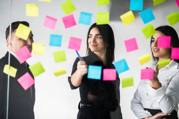 Jonge mannelijke en vrouwelijke collega's resterende notities schrijven voor collega's planning productieproces werken op kantoor. Studenten maken van memo stickers met takenlijst te organiseren dagindeling glimlachen — Stockfoto