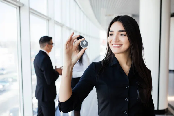 Blockchain y concepto de inversión. Líder mujer de negocios sosteniendo litecoin frente a su equipo con las manos en alto en la oficina . —  Fotos de Stock